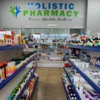 Interior of the Holistic Pharmacy showing aisles stocked with various vitamins, supplements, and over-the-counter medications. A sign on the back wall reads "Holistic Pharmacy Ltd. Premium Affordable Healthcare" above the pharmacist's counter.