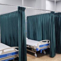 A clinical recovery area with three hospital beds arranged in parallel. Each bed is separated by floor-to-ceiling dark teal privacy curtains suspended from a silver metal ceiling track.