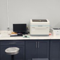A laboratory workspace featuring a white marble-patterned countertop with several automated diagnostic machines, including Mindray and Scil models. A central computer monitor and keyboard are set up for data entry.