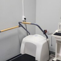 A close-up of a medical-grade treadmill used for diagnostic testing, located next to a white mobile cart holding a computer monitor, keyboard, and patient lead wires.